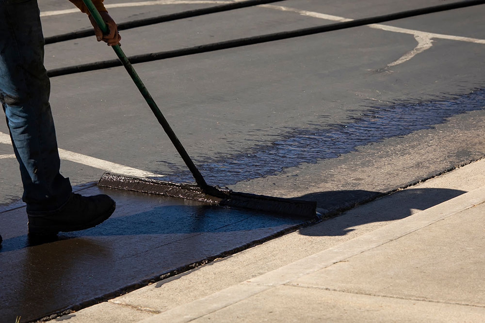 Worker using a sealcoating brush during asphalt resurfacing proj
